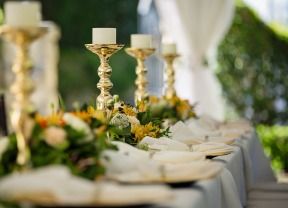 Elegant banquet table with white linens, gold candlesticks, and floral centerpieces at an outdoor event