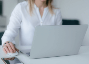 Person using a laptop at a white desk, with a smartphone beside them