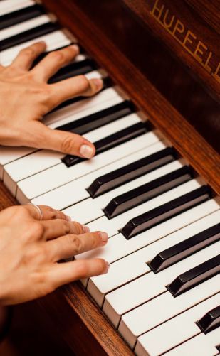 Hands playing a piano keyboard with a wooden frame and visible brand name.