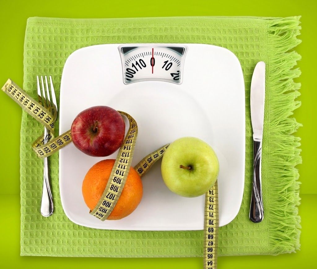 Una bilancia circondata da frutta su una tovaglietta verde, a suggerire un'alimentazione sana o una dieta.