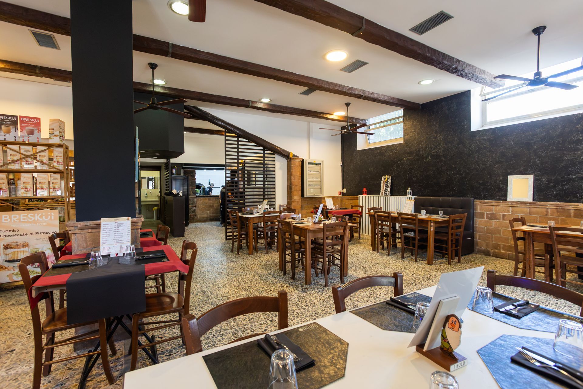 Luminoso interno del caffè con tavoli, sedie, scale e ventilatori a soffitto in legno.