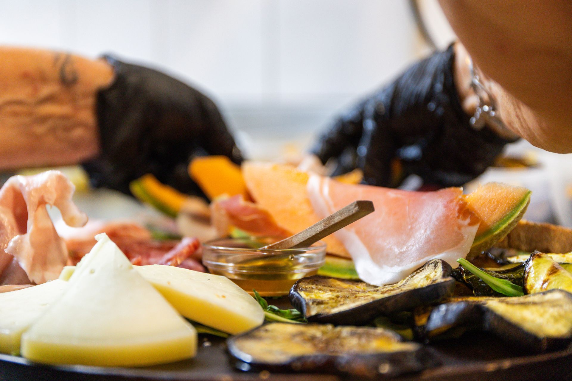 Mani che dispongono vari alimenti affettati e verdure su un piatto con una piccola ciotola di salsa