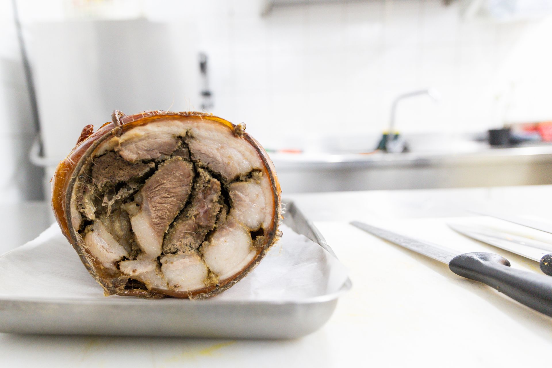 In una cucina luminosa, un rotolo di maiale ripieno a fette è disposto su un vassoio, con un coltello accanto.