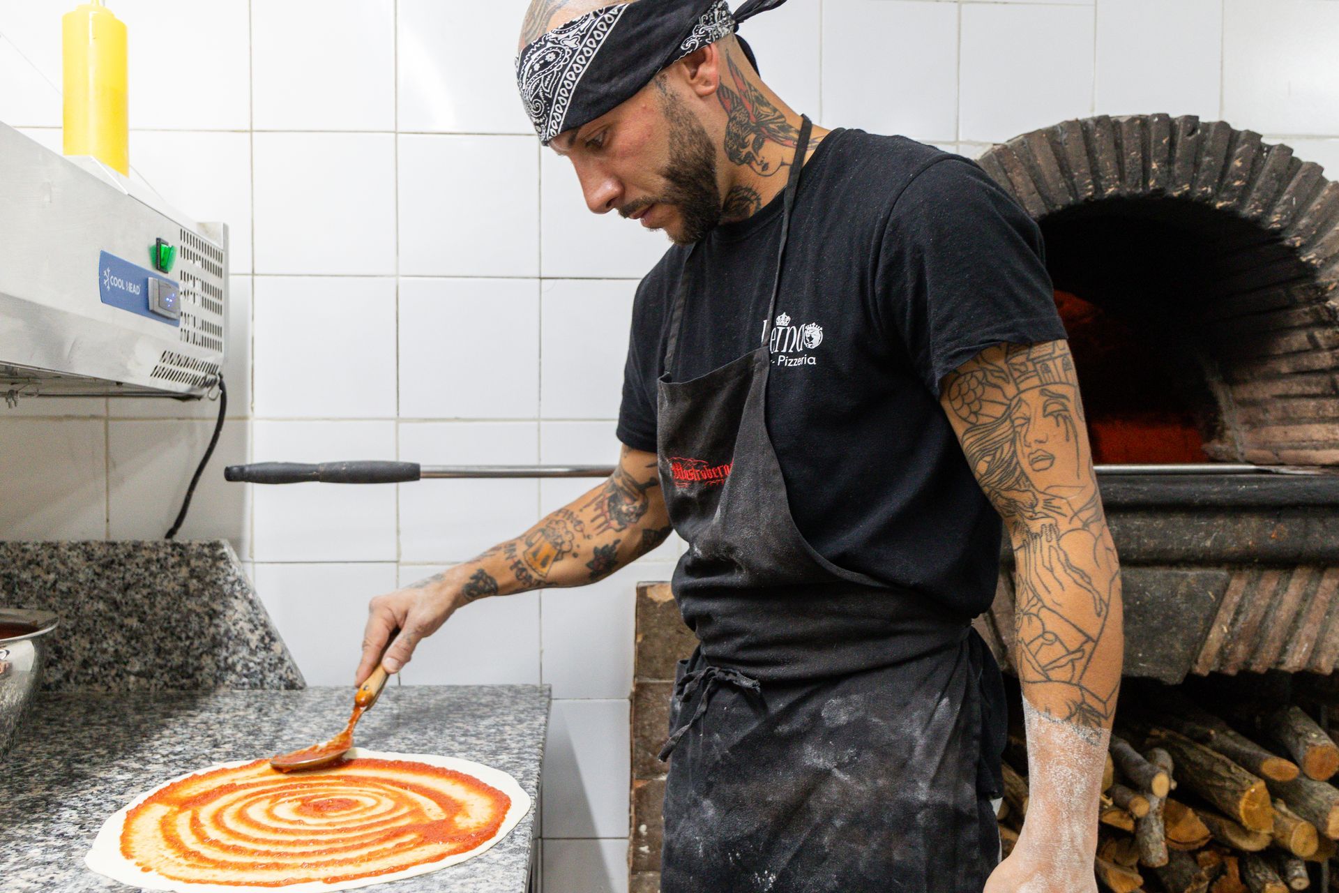 Lo chef stende la salsa su una pizza in una cucina con forno a legna.