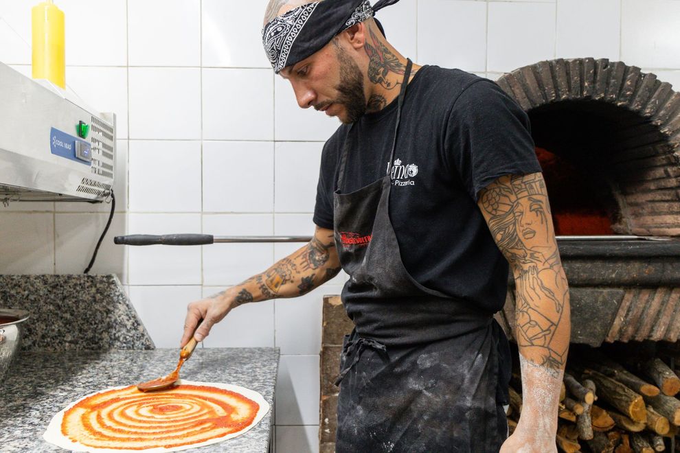 Lo chef stende la salsa su una pizza in una cucina con forno a legna.
