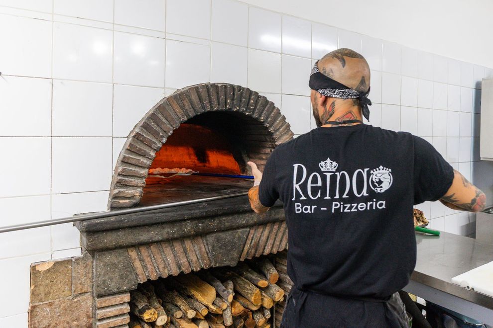 Lo chef si occupa di un forno a legna nella cucina piastrellata della pizzeria Rina Bar-Pizzeria.