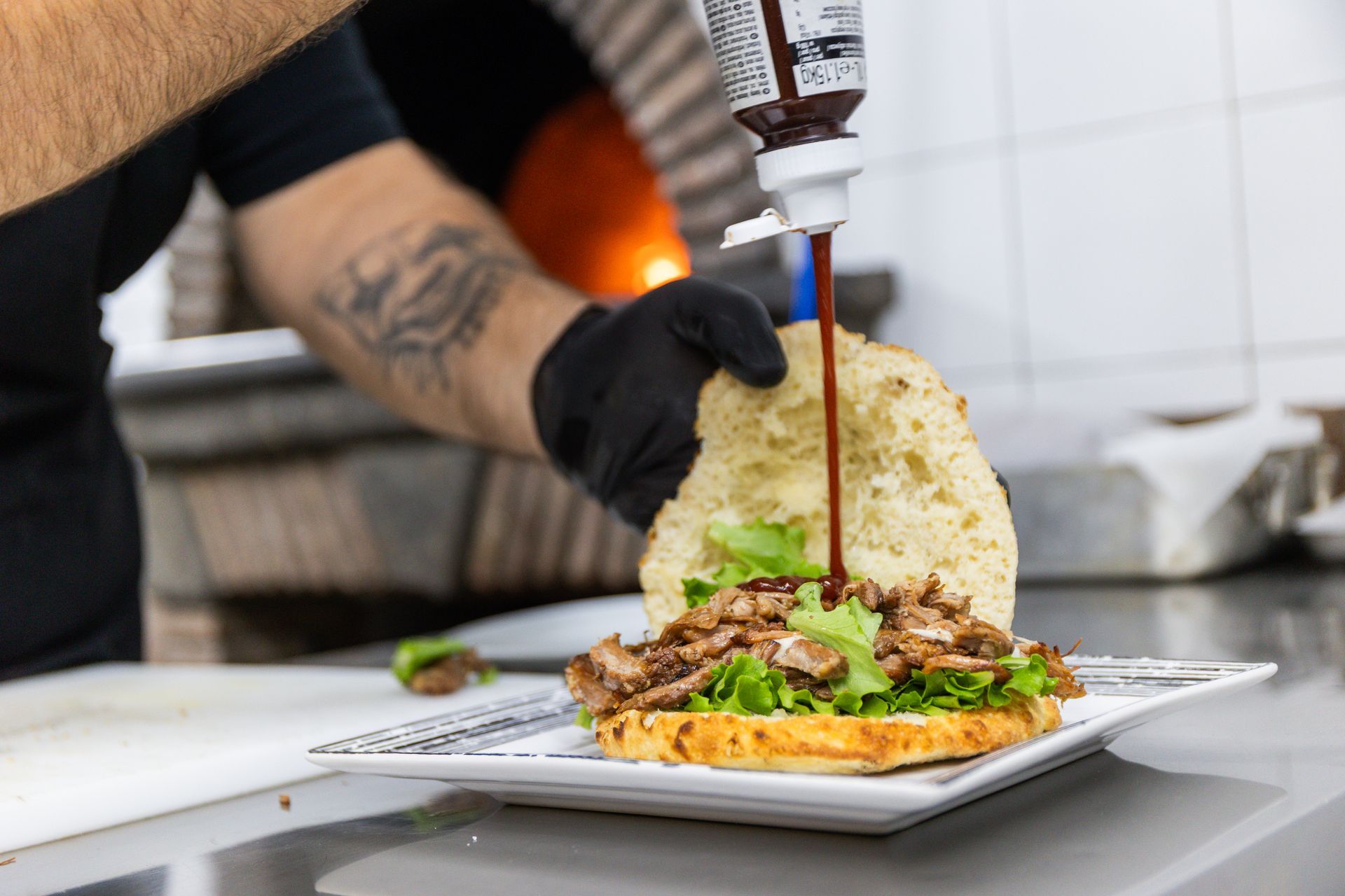 Lo chef decora un hamburger con la salsa su un bancone della cucina.