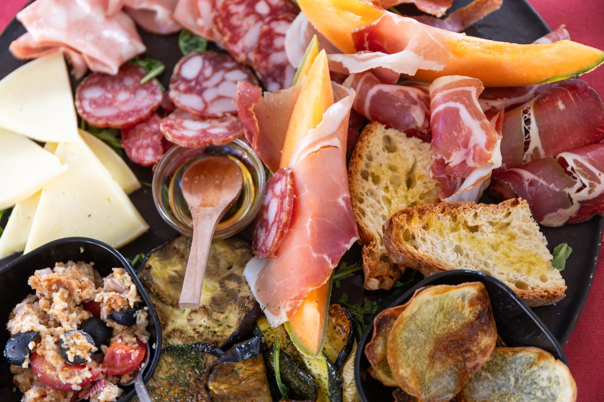 Tagliere di salumi con affettati, formaggi, pane, olive e frutta secca su un piatto nero