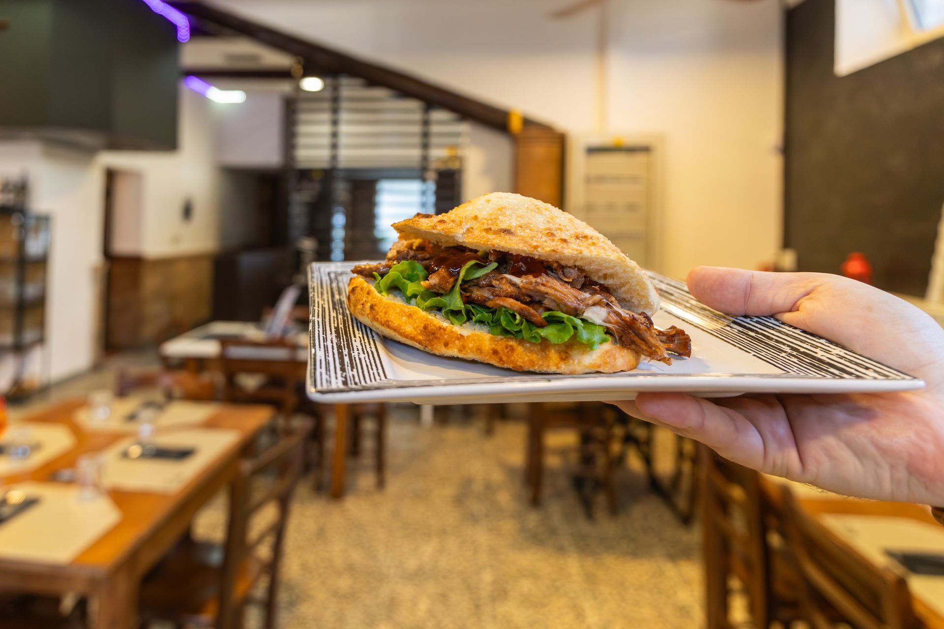 Un panino su un piatto decorato, tenuto in un ristorante, con tavoli e sedie sfocati sullo sfondo.