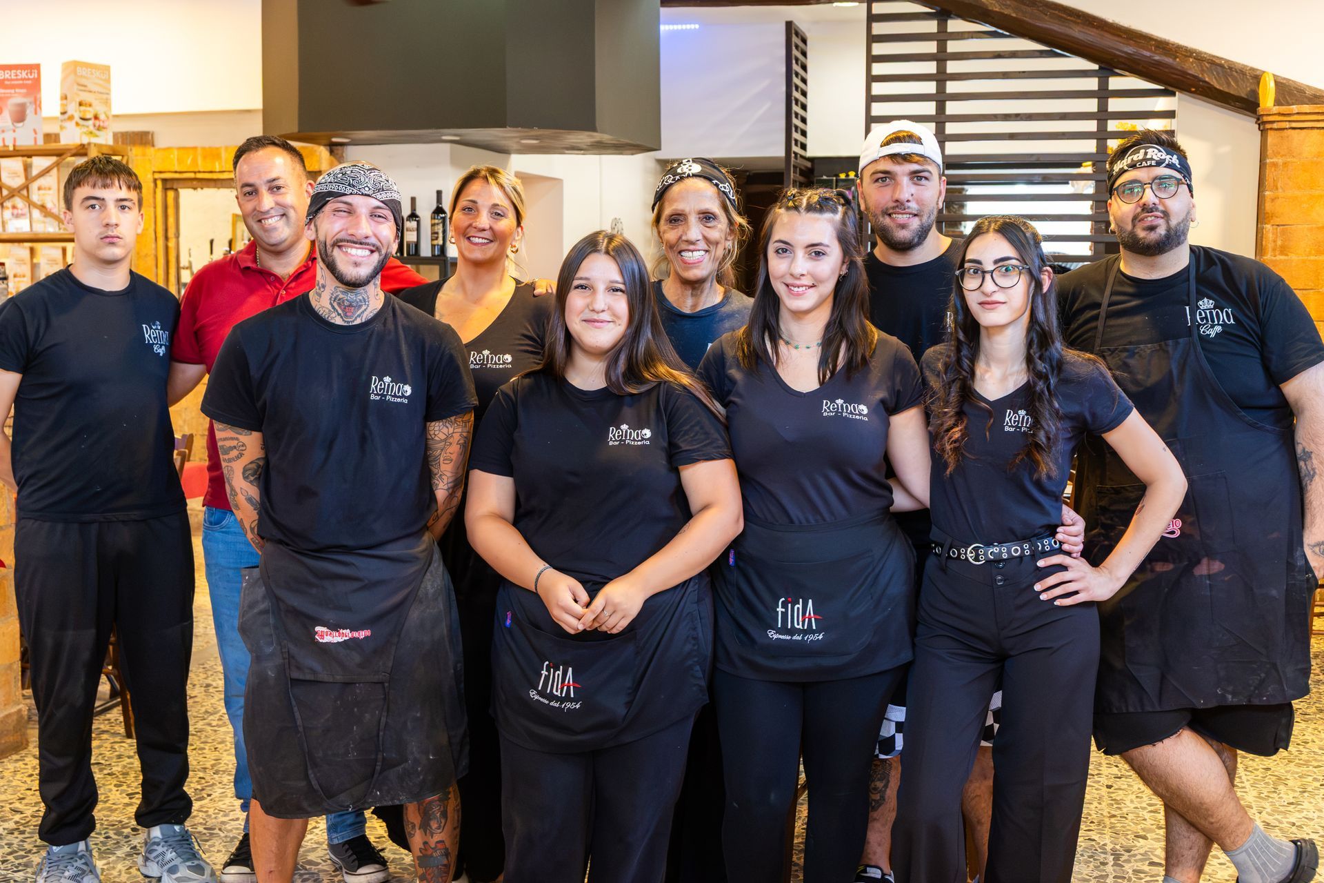 Un gruppo di dipendenti di un ristorante in uniforme nera, in piedi all'interno, sorridono alla telecamera.
