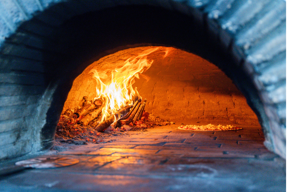 Fuoco ardente che arde all'interno di un forno o di una fornace in pietra blu, con fiamme e braci visibili.