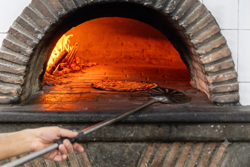 Mano che usa una pala di metallo per regolare un forno a legna con fiamme ardenti all'interno