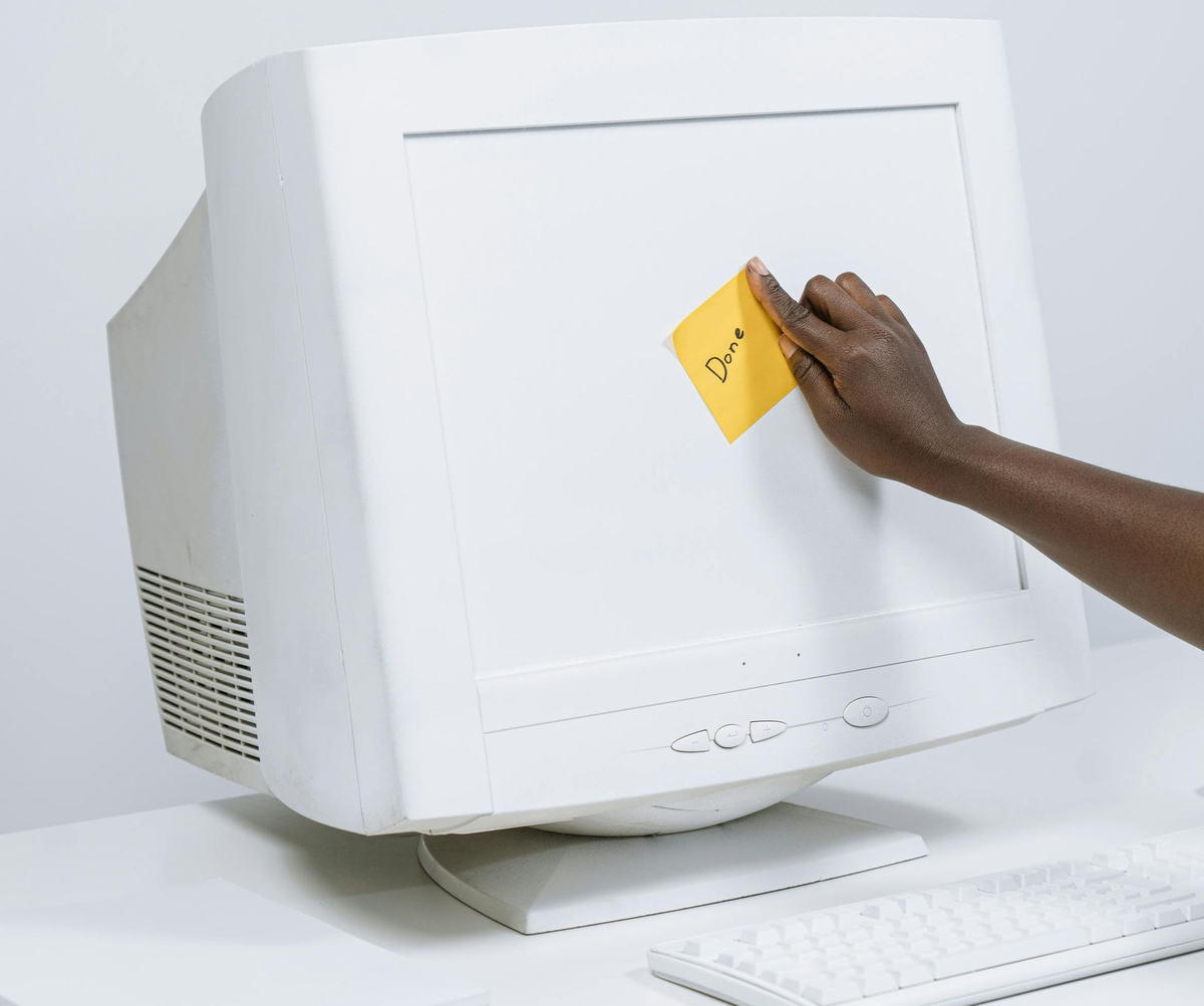 A hand sticking a yellow note marked Done onto an old white computer monitor
