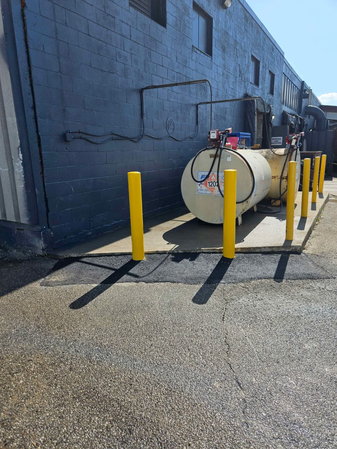 A fuel tank is parked in front of a building next to yellow poles.