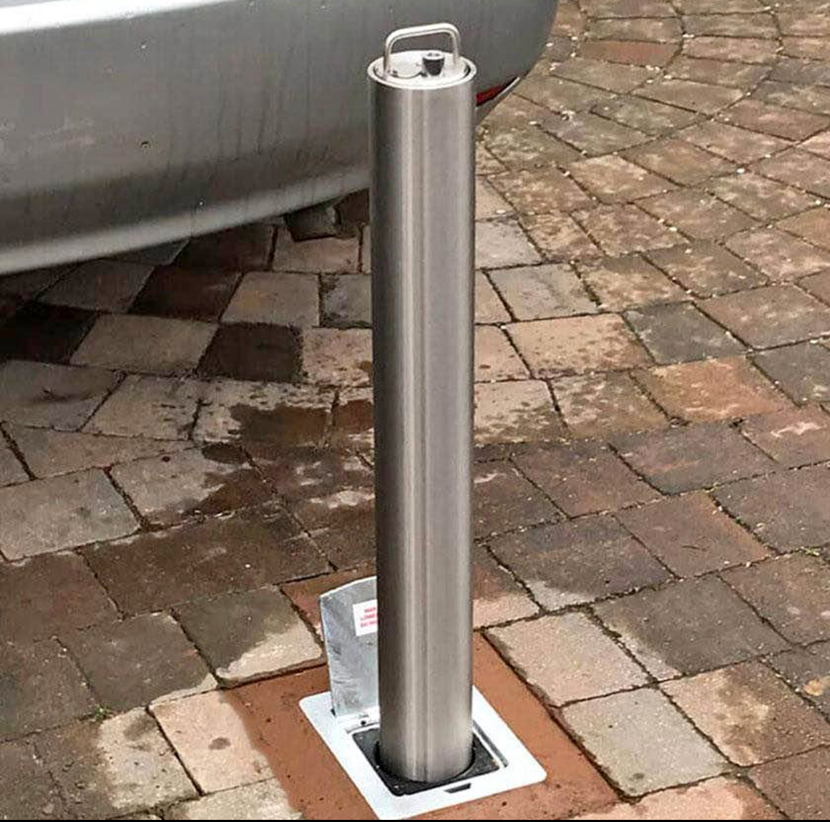 A silver car is parked next to a stainless steel pole on a brick driveway.