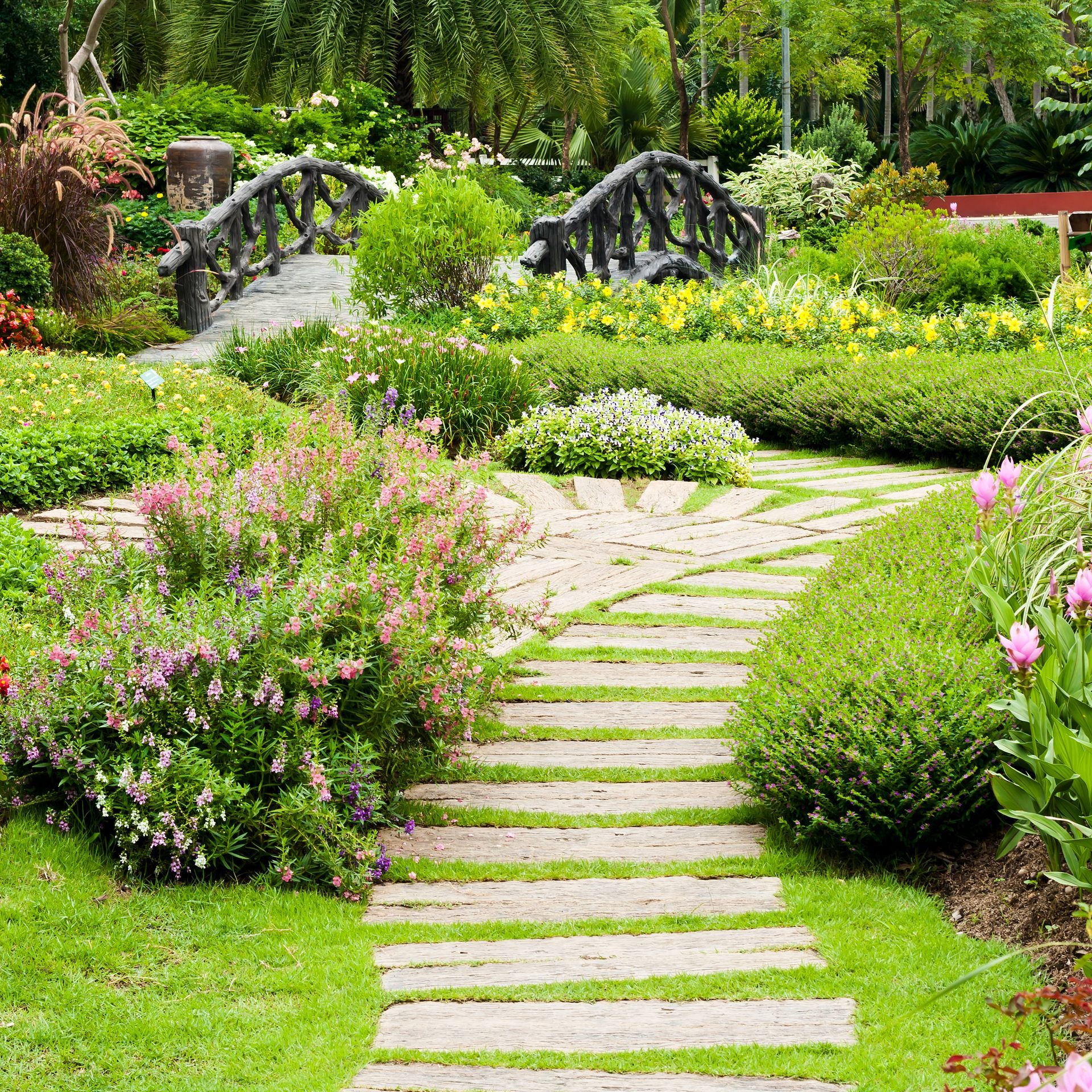 A path in a garden with flowers and a bridge.