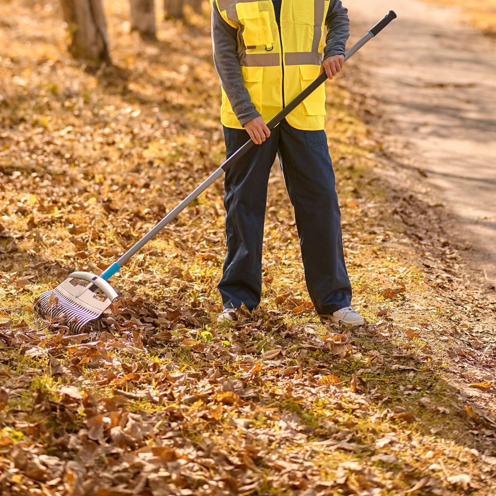 A man in a yellow vest is raking leaves on the ground