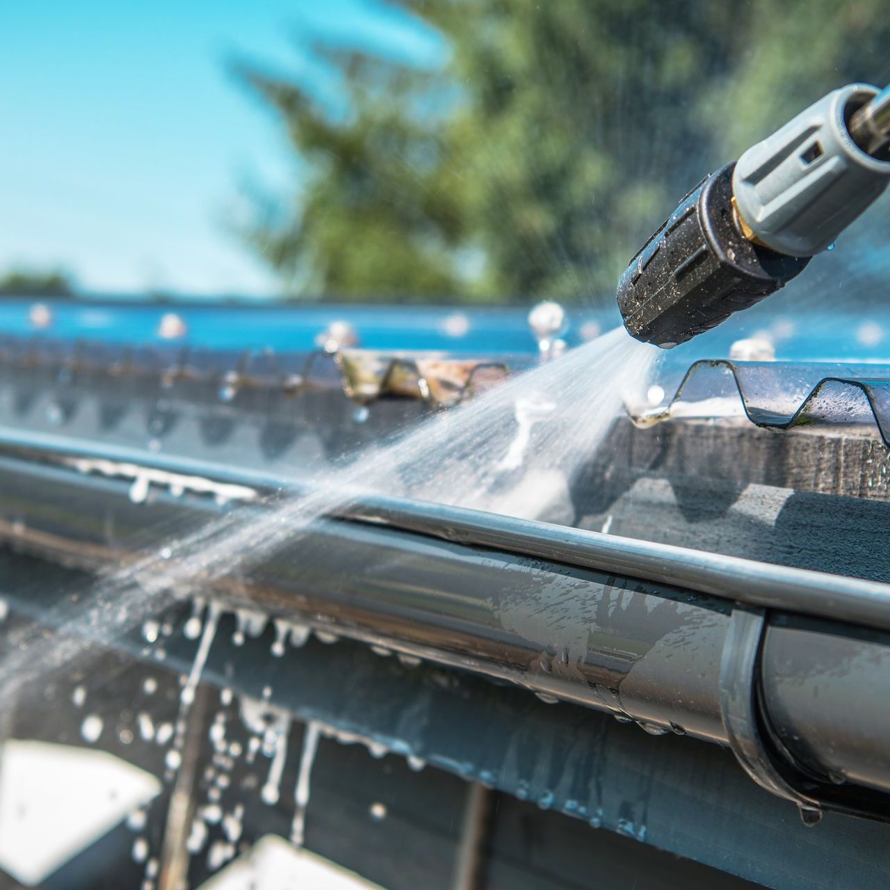 A person is using a high pressure washer to clean a gutter on a roof.
