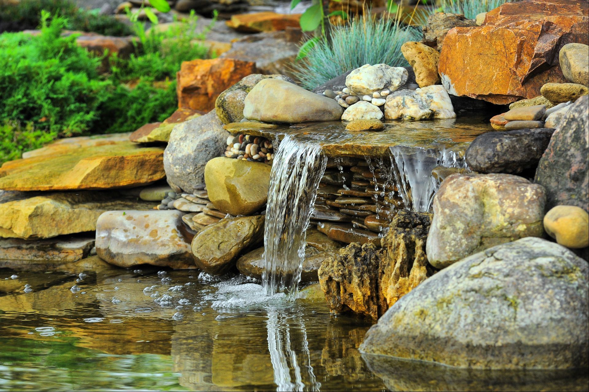 A small waterfall is surrounded by rocks in a pond.