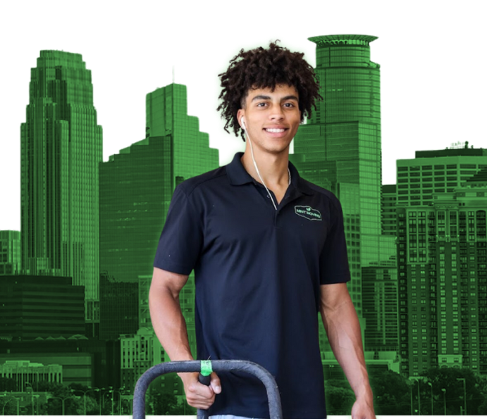 Man in black polo shirt holding equipment, with green city skyline in background.