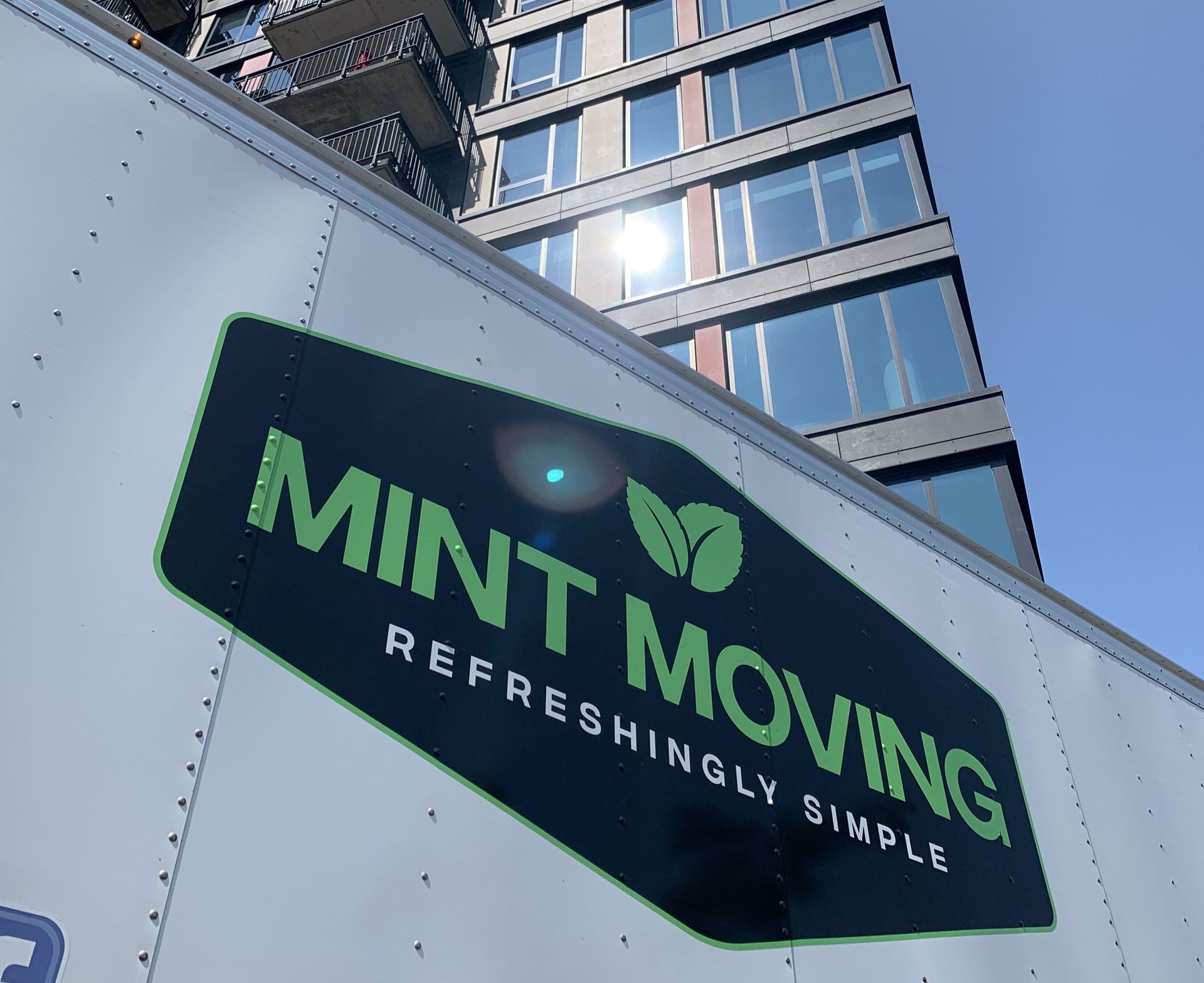 Mint Moving truck with logo in front of a modern building.