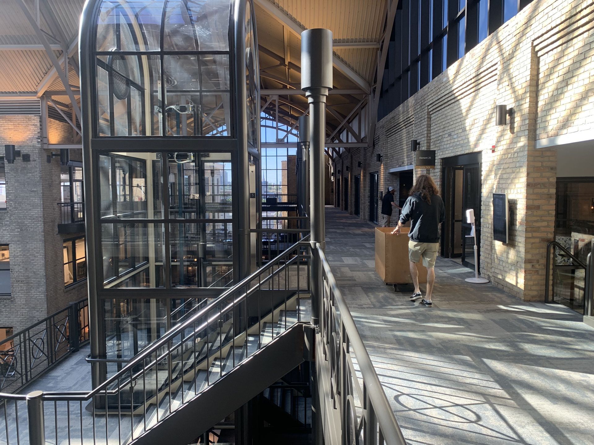 A person walks down a second-story hallway with an elevator on the left.