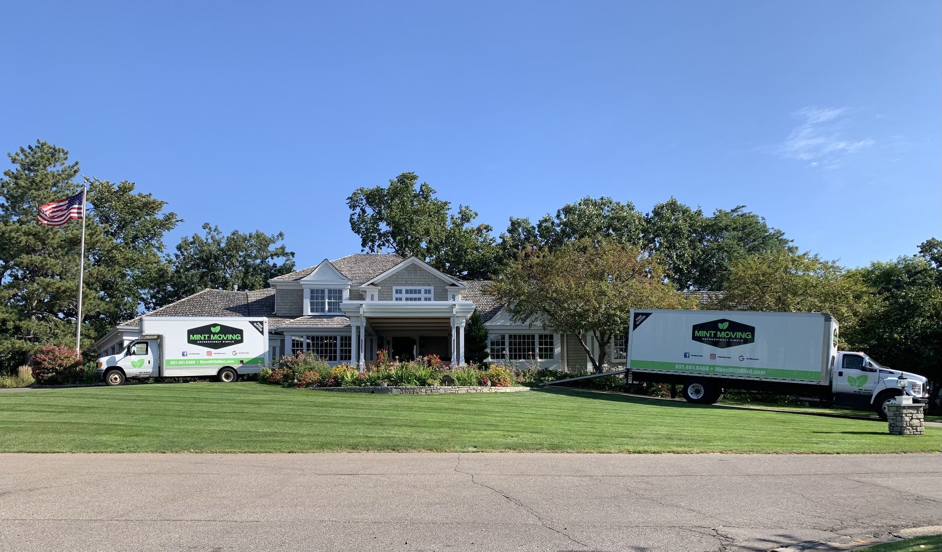 Two moving trucks parked in front of a light gray house on a sunny day.