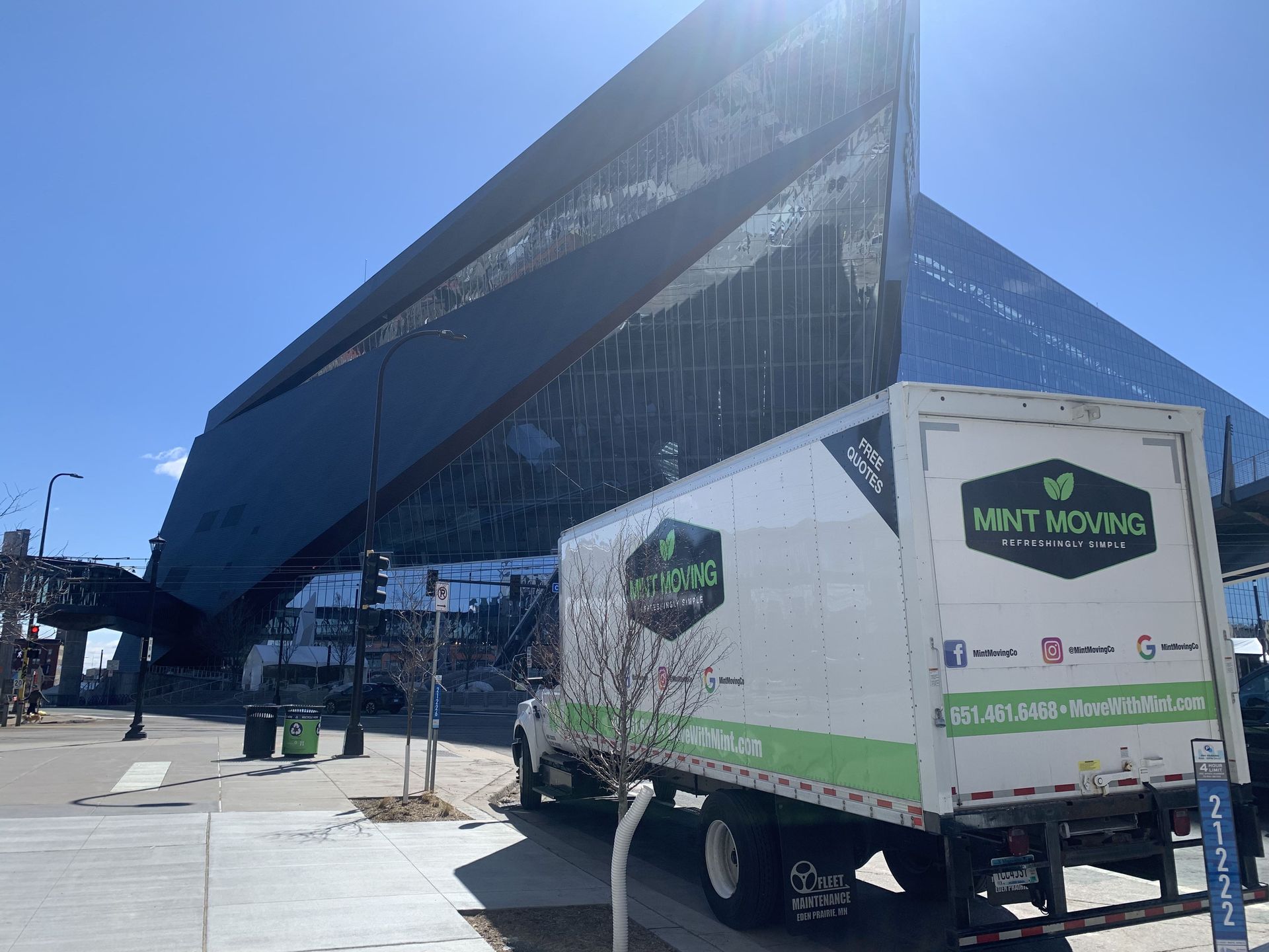 Moving truck in front of a modern, dark-glass building, with a sunny, blue sky.
