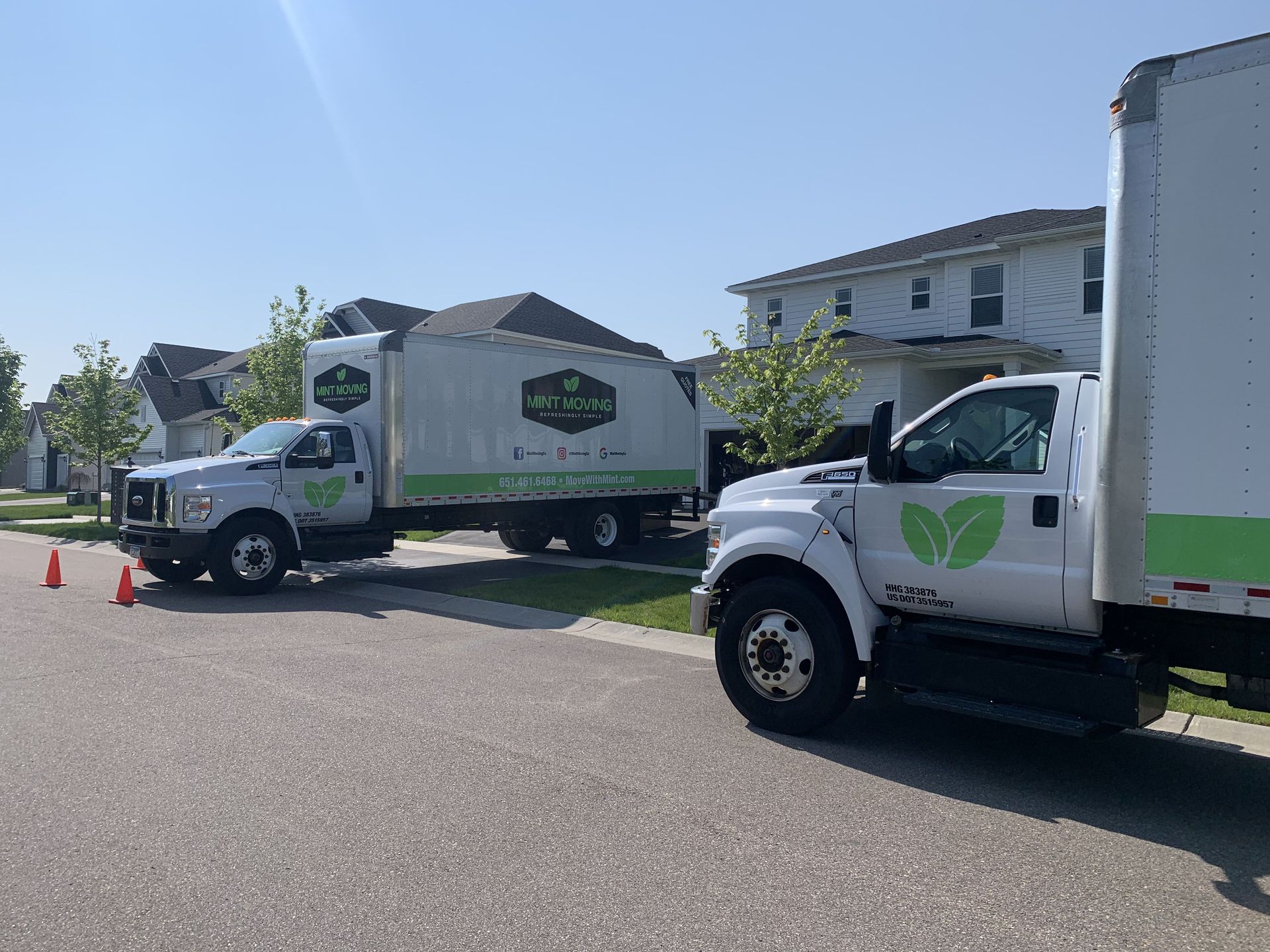 Two white box trucks parked on a residential street with green logos.