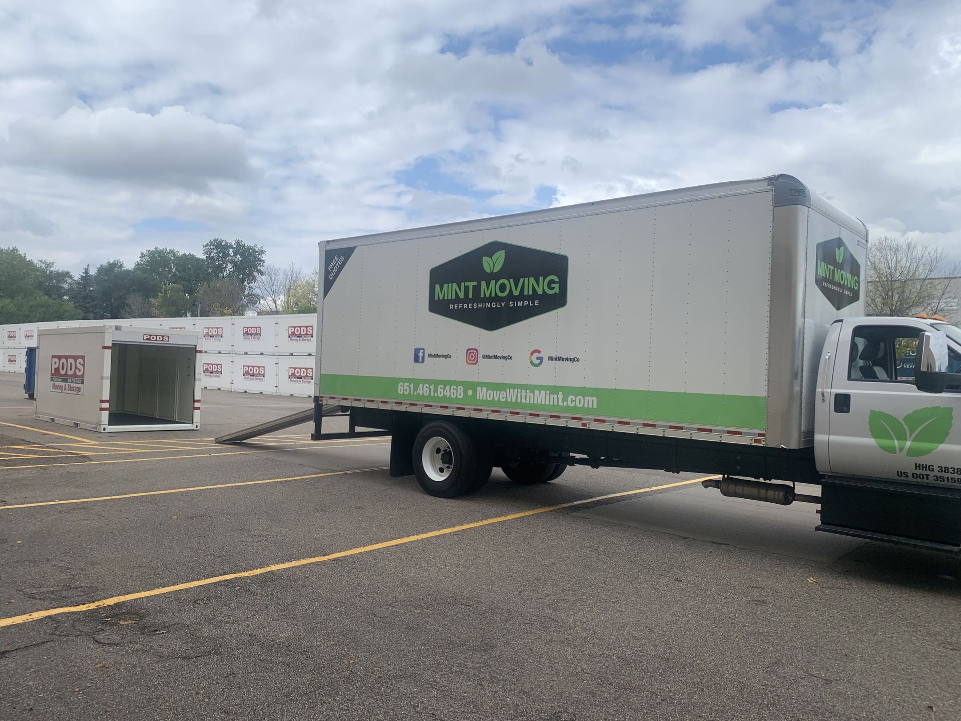 Mint Moving truck parked near storage units. Truck is white with green accents, ramp deployed.