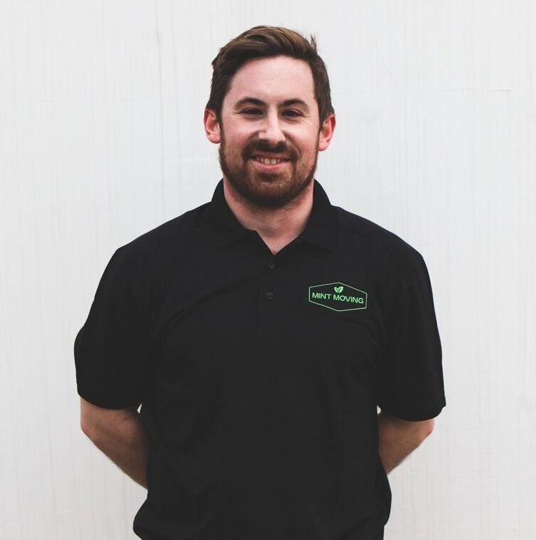 Man with beard, in black polo shirt with green logo, smiling in front of a white wall.
