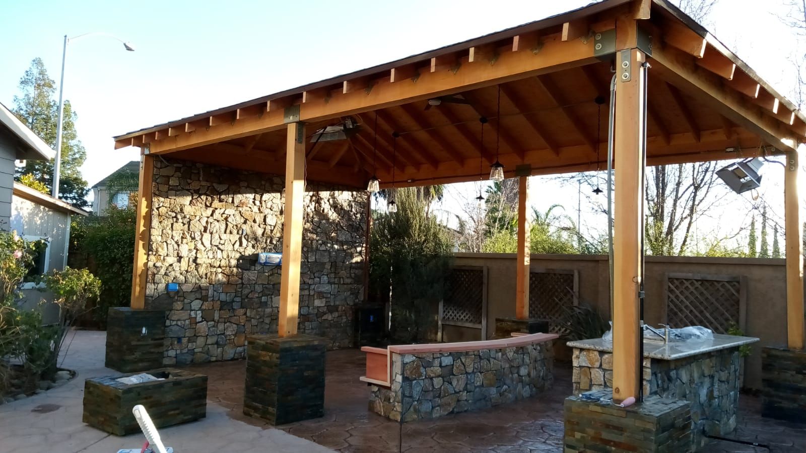 Rustic stone patio with wooden roofed pavilion, built-in grill, and outdoor seating area