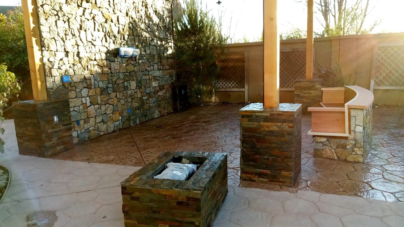 Outdoor patio with stone planters, a bench, and a paved walkway in sunlight