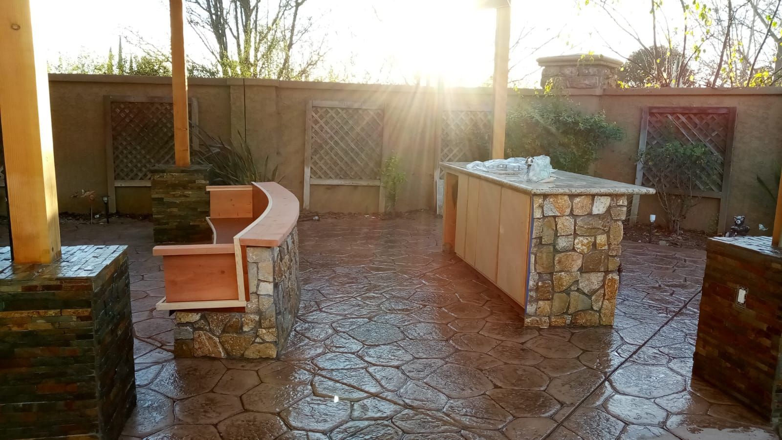 Sunlit stone patio with built-in benches and a long counter, surrounded by a low wall and plants