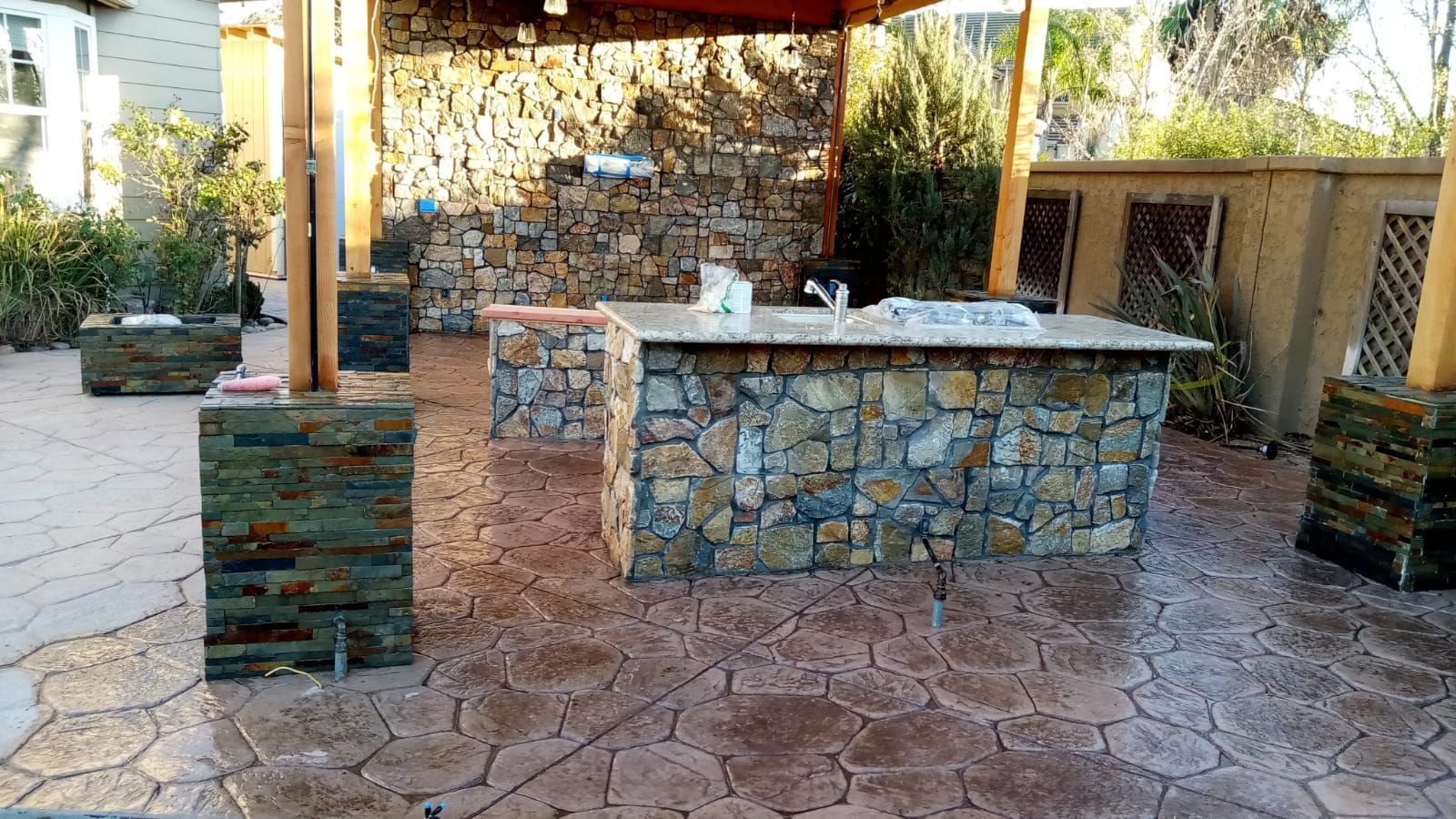 Stone outdoor patio with a built-in grill and bar under a shaded pergola