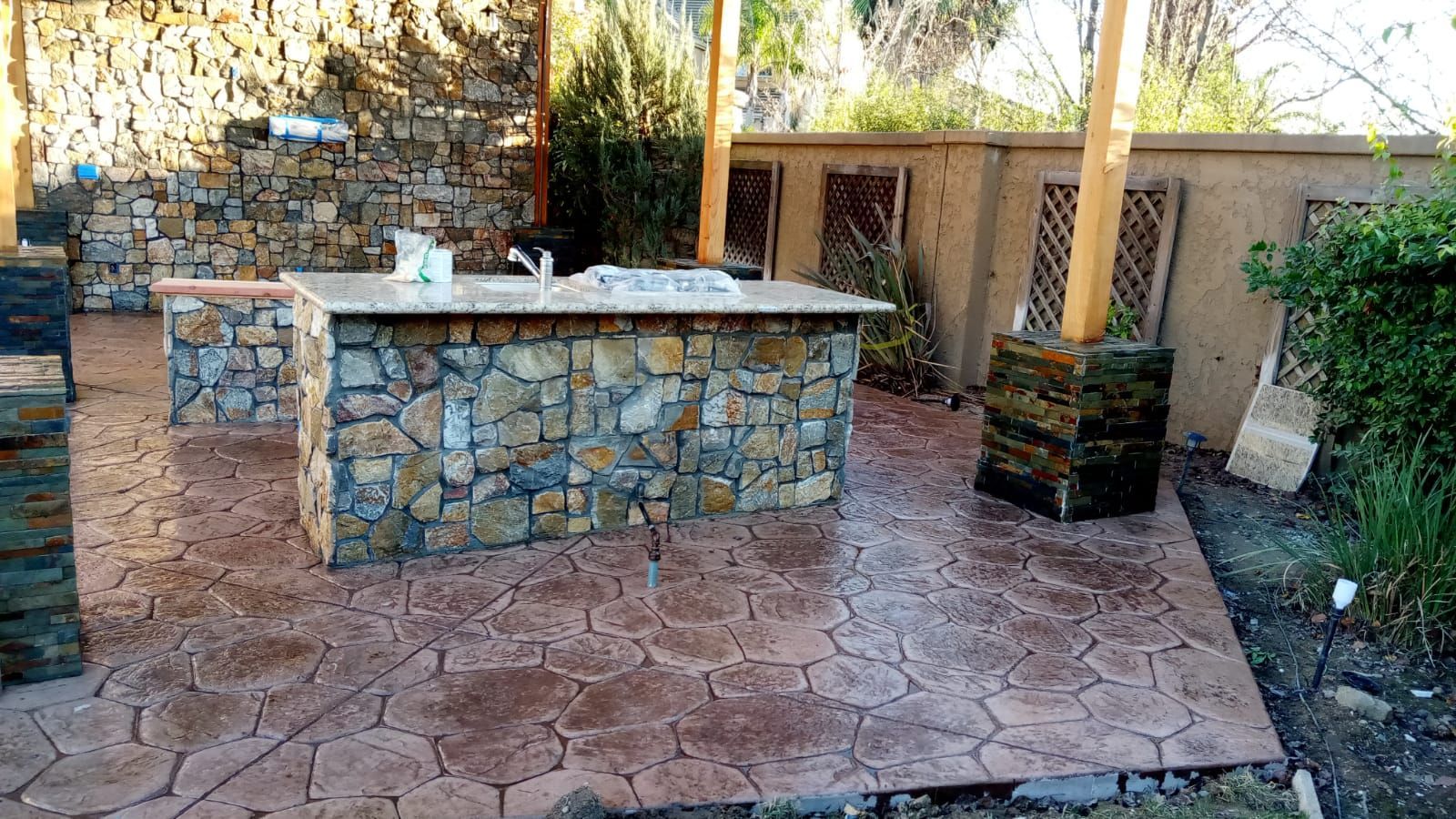 Stone patio with built-in outdoor barbecue grill beside a small landscaped yard and wall