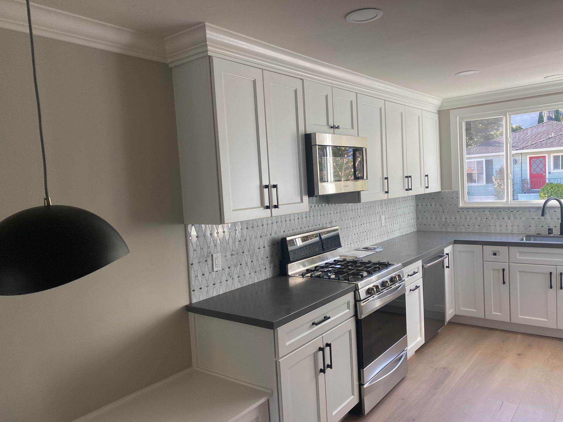 Bright modern kitchen with white cabinets, gray countertops, stainless appliances, and a window over the sink