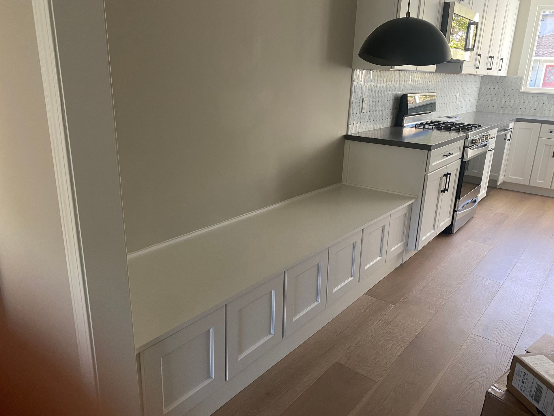 Built-in white cabinets along a hallway leading to a bright kitchen with black pendant light and wood floors