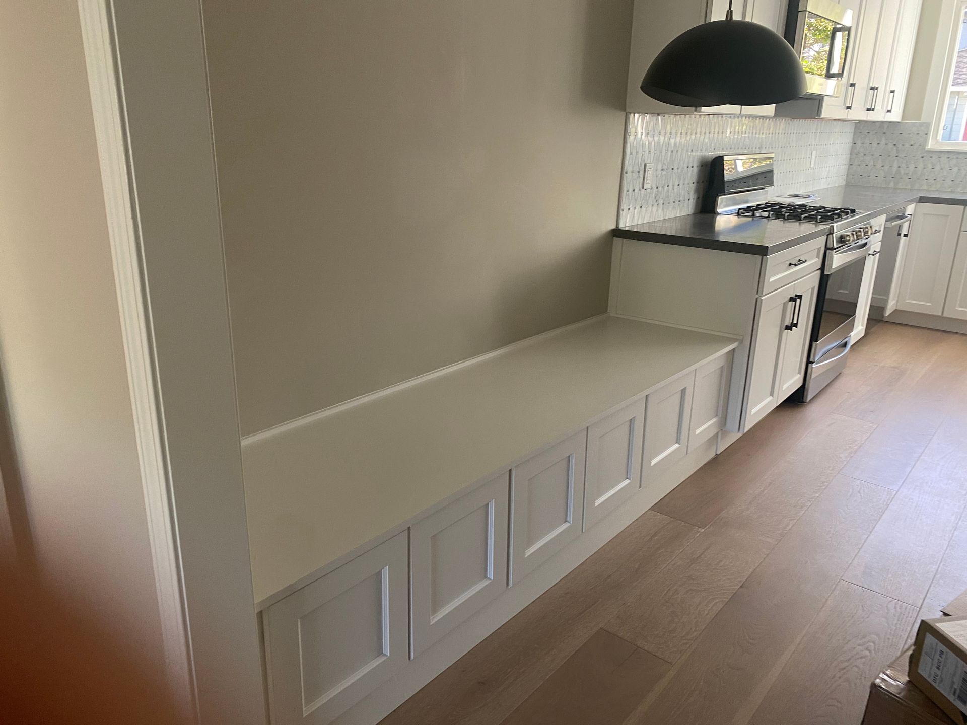 Modern kitchen with white lower cabinets, wood floor, and a black pendant light by the counter.