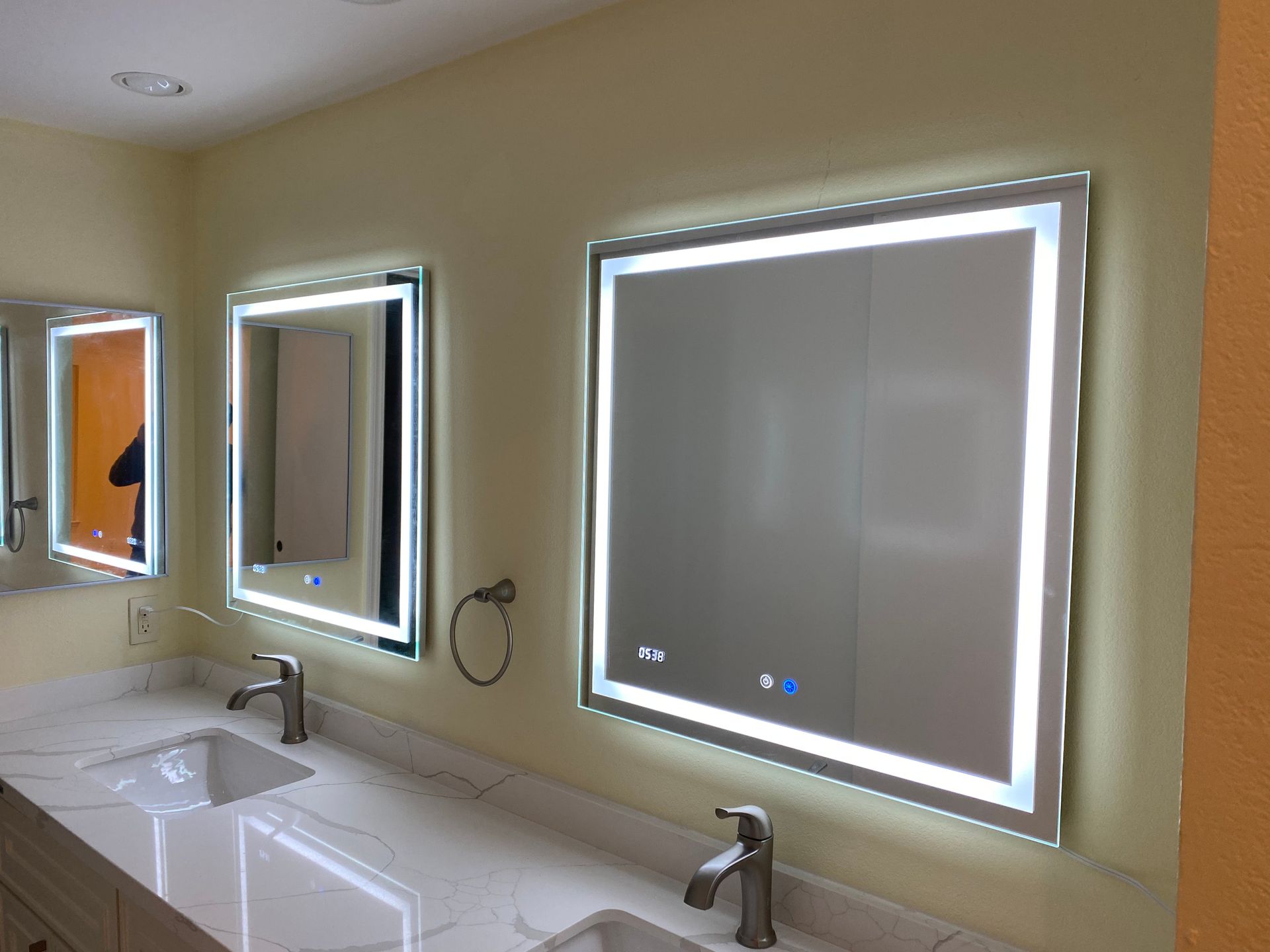 Bathroom vanity with two lit mirrors, double sinks, and beige walls