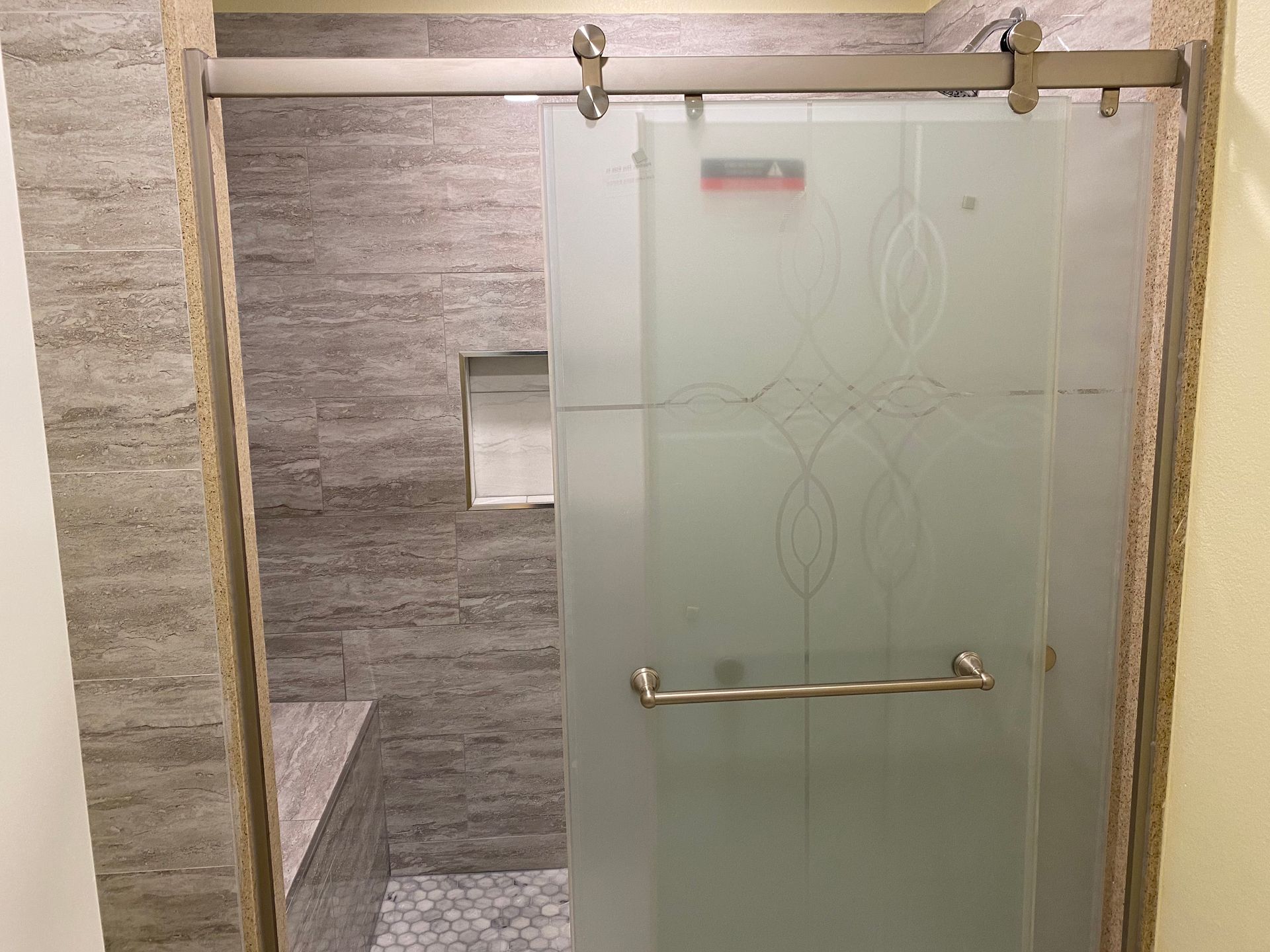 Shower with frosted glass door, chrome handle, and gray tiled walls in a bathroom