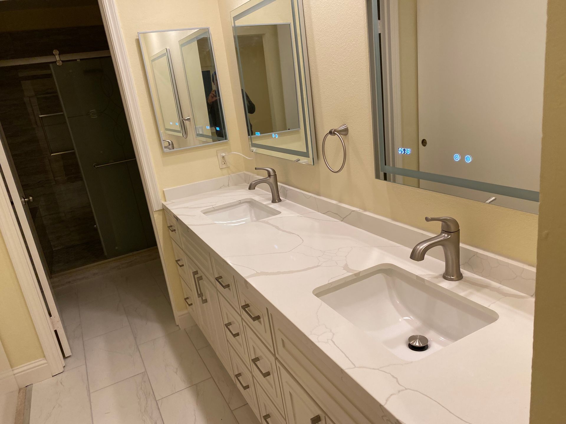Bathroom vanity with double sinks, mirrors, and beige tile flooring.