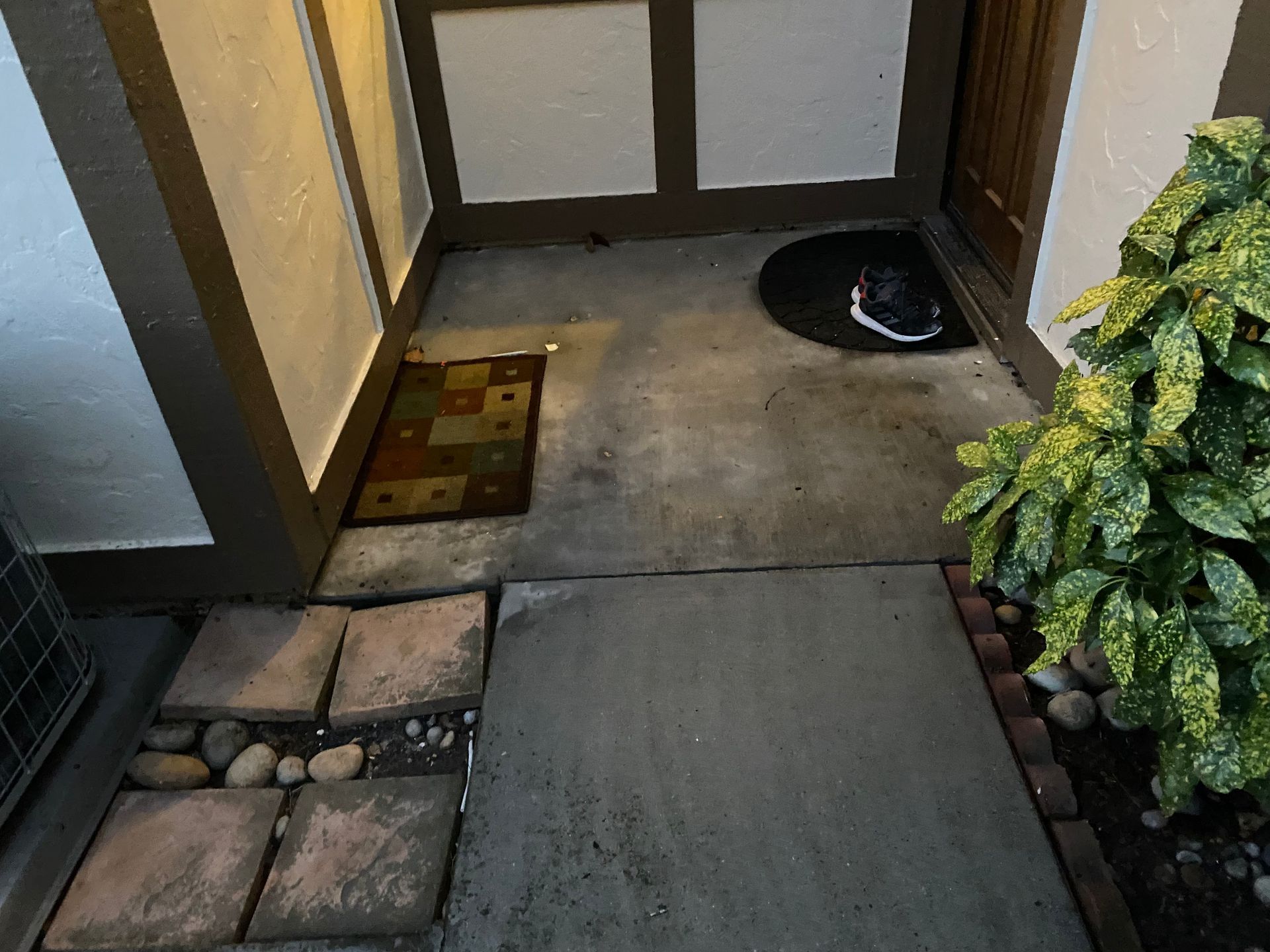 Front walkway with stepping stones, concrete path, doormat, and potted greenery by a house entrance.
