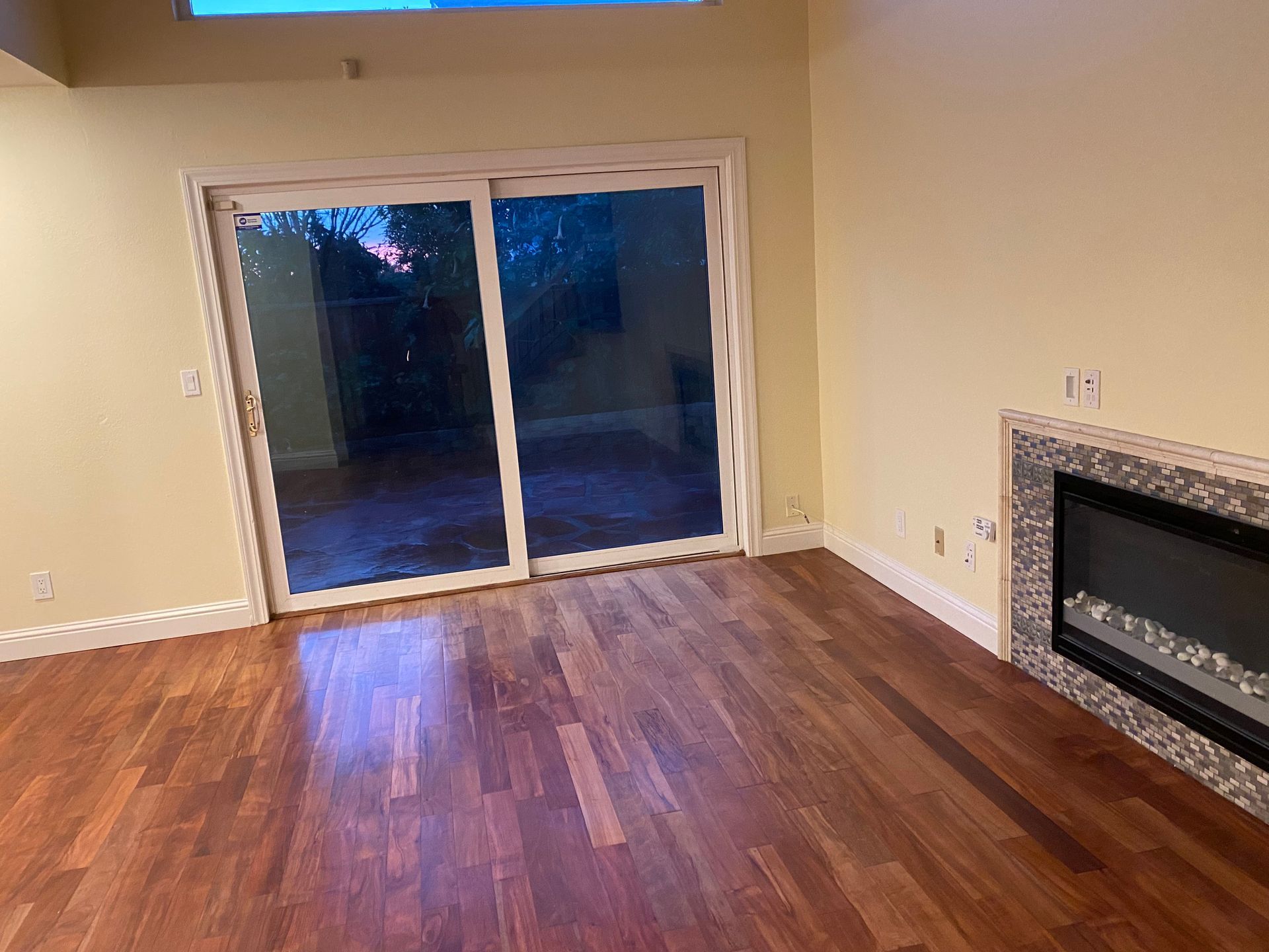 Empty living room with hardwood floors, fireplace, and sliding glass doors to a dark outdoor patio