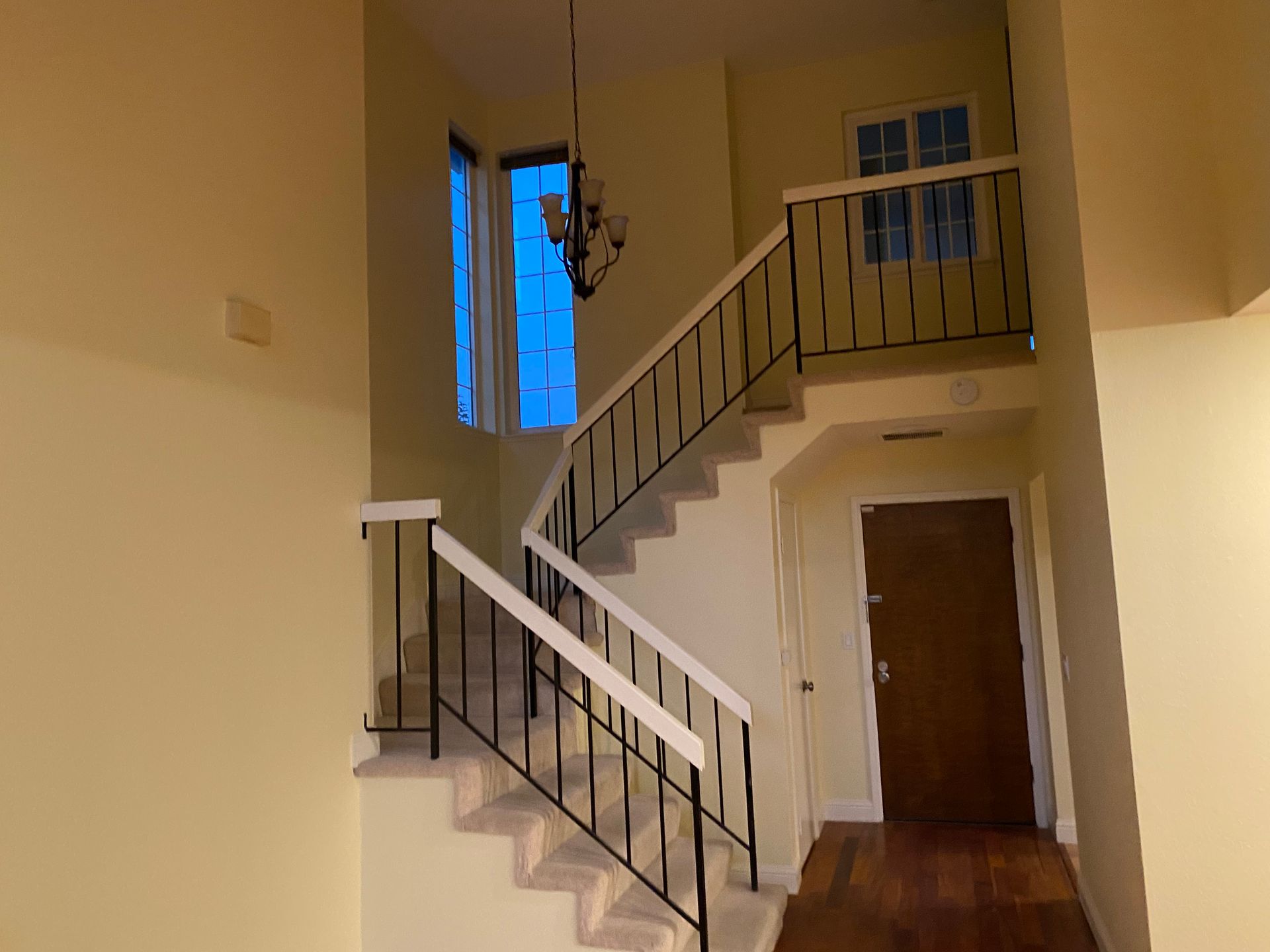 Indoor stairwell with white railings, brown door, and blue-lit window on a beige wall.
