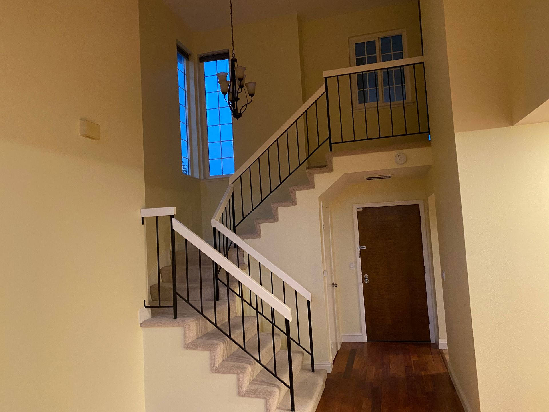Interior staircase with white railings, wooden floors, and a brown front door in a beige entryway.