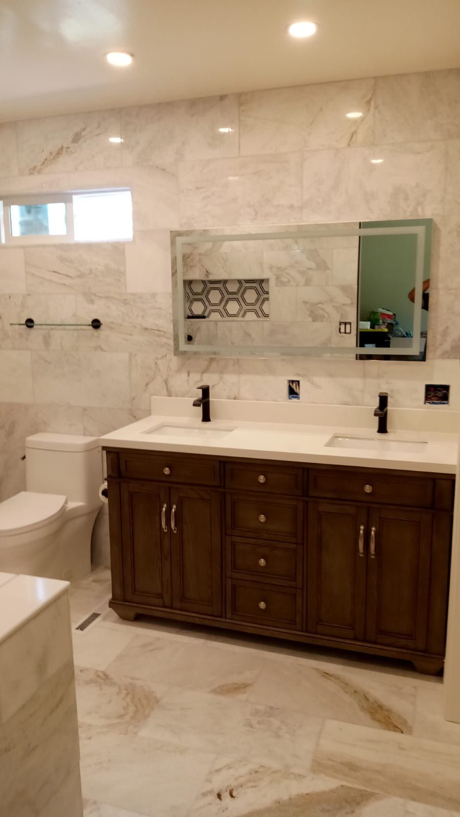 Modern bathroom with marble walls and floor, dark wood vanity, double sinks, and a toilet.