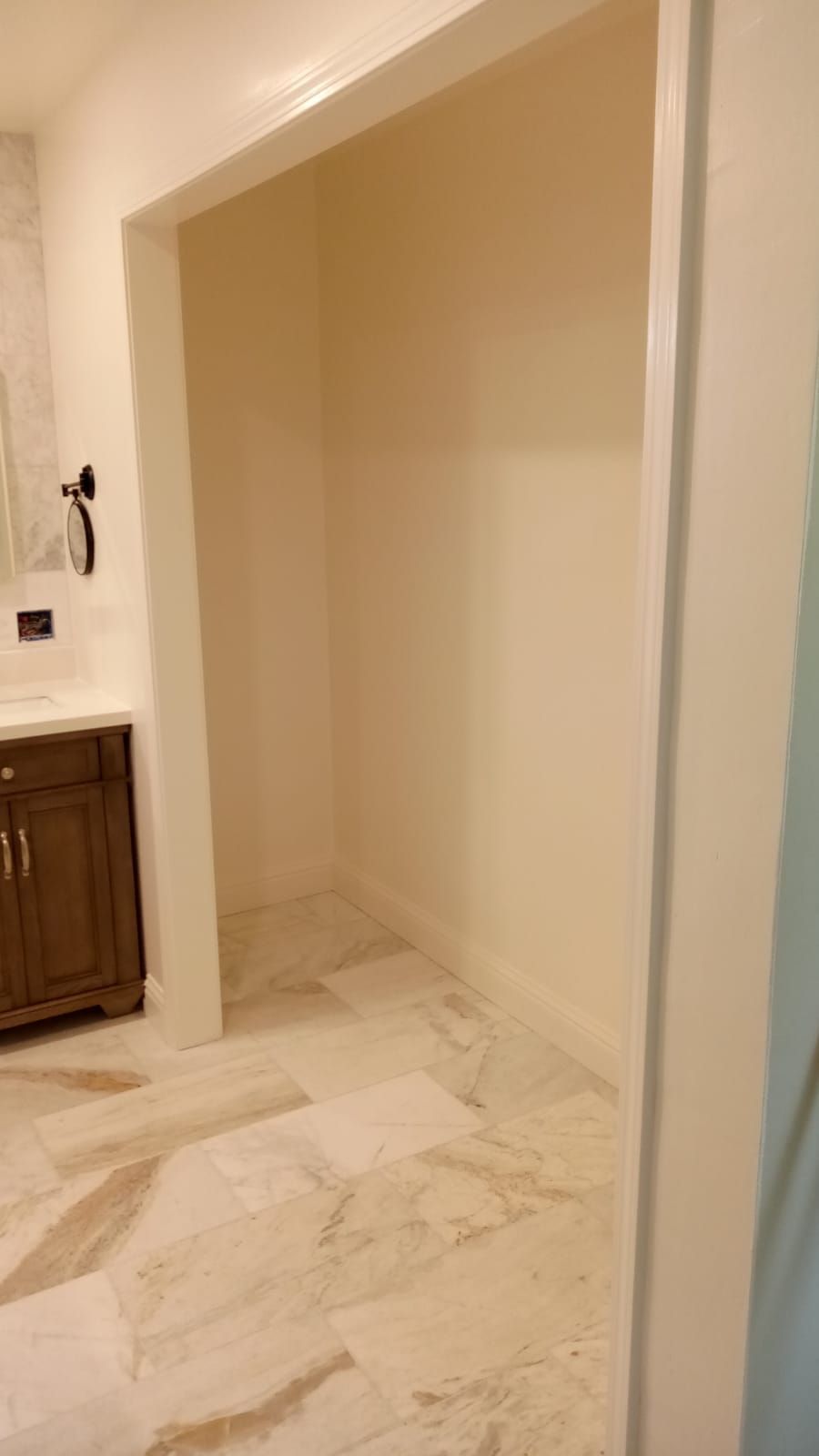 Empty beige closet or alcove with marble tile floor beside a bathroom vanity