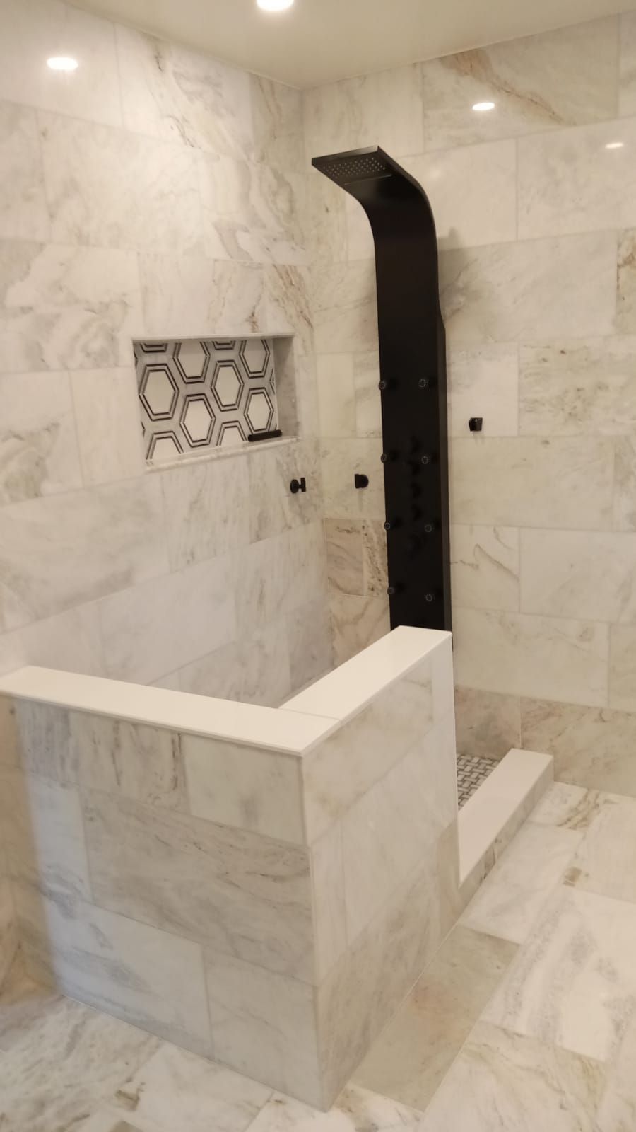 Marble-tiled shower with a black curved showerhead and built-in bench