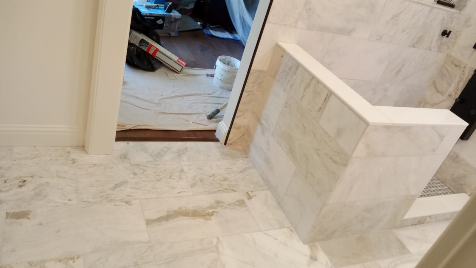 Tiled hallway with a step-down doorway leading to a cluttered room, and a raised marble half-wall on the right